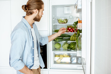 Young vegan man choosing what to cook, taking fresh vegetables from the refrigerator at home