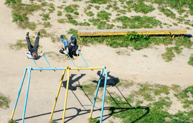 An aerial view of two Caucasian boys carelessly swinging on a swing set over background of a...