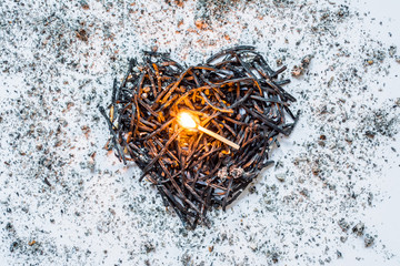 Heart symbol made of burned-down matches close-up with a burning match in the center and ashes around. The concept of the complexity of love relationships, unhappy love.