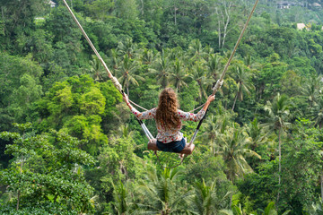 Woman with long curly hair swinging in the jungle, Bali. Rain forest on the background