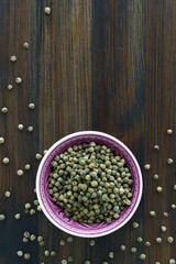 Dried green peppercorns in a violet bowl. Dark wooden table, high resolution