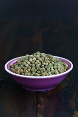 Dried green peppercorns in a violet bowl. Dark wooden table, high resolution, negative space