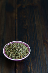 Dried green peppercorns in a violet bowl. Dark wooden table, high resolution, negative space
