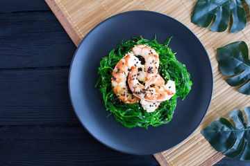 Salad with seaweed and red shrimps in the dark plate on the tropical background.Top view.Closeup.Copy space.