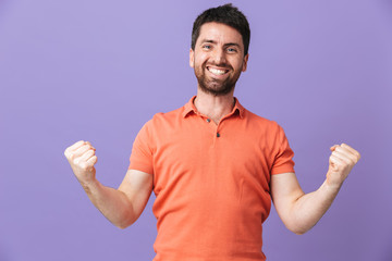 Happy young handsome bearded man posing isolated over violet purple wall background make winner gesture.