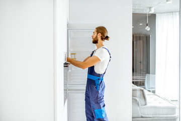 Fototapeta na wymiar Handsome workman installing new refrigerator in the modern kitchen at home