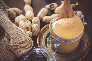 Peanut Butter in Glass Jar with Peanuts in Shell on Wooden Background. Vegetarian Food Concept.