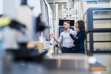 Businessman and businesswoman talking at a machine in modern factory