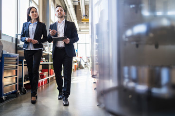 Businessman and businesswoman with tablet walking and talking in a factory