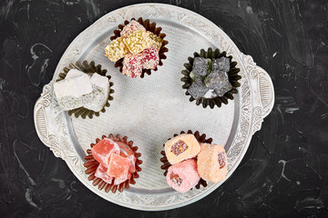 Set of various Turkish delight in traditional silver bowl on metal tray black background.Middle Eastern dessert. Top view. Flat lay