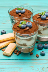 Classic tiramisu dessert in a glass with blueberries on blue wooden background