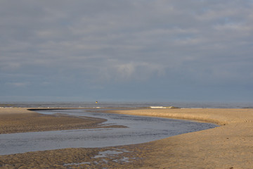 Białe pogodne chmury na niebieskim niebie ponad nadmorską plażą.