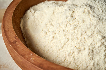 Closeup of flour in wooden bowl on a white table.
