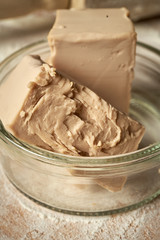 Closeup of fresh yeast in glass bowl on wooden table.