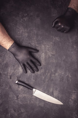 Big Knife and Male Hands with Black Latex Gloves on Dark Background