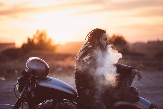 Side view of man smoking electronic cigarette on motorbike during sunset