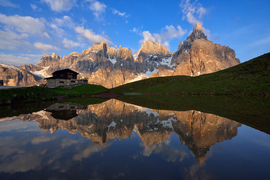 Italy, Trentino, Dolomites, Passo Rolle, Pale di San Martino range, Cimon della Pala with Baita Segantini reflecting in small lake in the evening