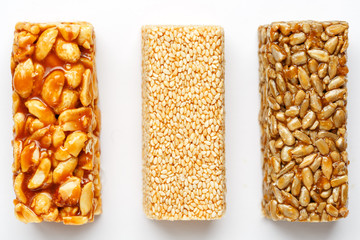 Grain granola bar with peanuts, sesame and seeds in a row on a white background. Top view Three assorted bars, isolate