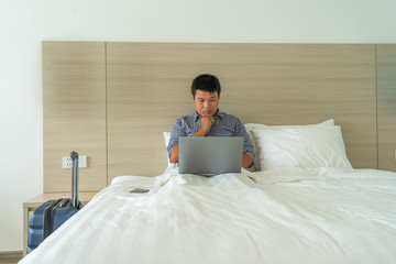 Businessman using laptop on bed next to suitcase in hotel