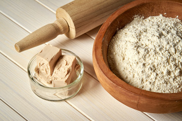 Top view of bowl of flour with yeast and rolling pin on  white  kitchen table