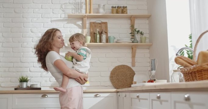 Pretty caucasian woman is babysitting with cute little baby boy, carrying him on hands, while doing everyday routine and positively smiling - lifestyle concept 4k
