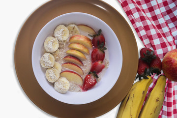 Oat Flakes with sliced bananas and honey, apples and strawberries in bowl. Wood background. Top view.
