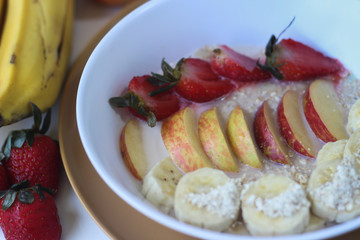 Oat Flakes with sliced bananas and honey, apples and strawberries in bowl. Wood background. Top view.