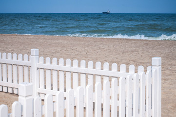 Elegant and simple white wooden fence on beach sand with sea surf background. Minimal summer...