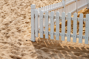 Retro style white painted wooden fence on beach sand with clear striped shadows. Minimal summer...
