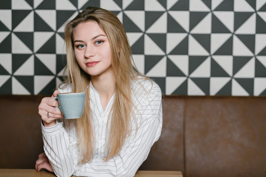 Pensive Woman with cup of fresh coffee looking at camera while sitting at table in cozy restaurant