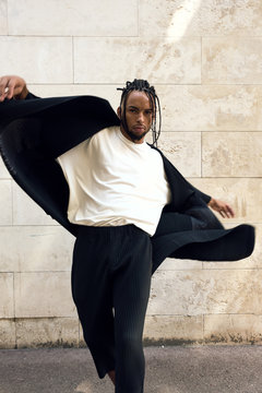 Fashionable young African American male in stylish outfit posing in street near grungy wall on sunny day on city street