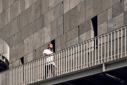 Young African American man walking on on bridge while spending time on city street on sunny day