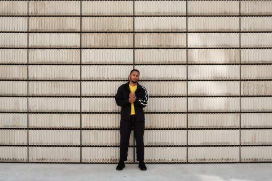 Young African American guy in trendy sportswear looking at camera while standing near cement blocks on city street