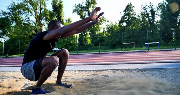 Slow motion close up of young african male athlete is performing a long jump on race track in athletics stadium in a sunny day.