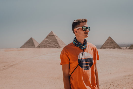 Confident male traveler in sunglasses looking away while standing in desert against famous Great Pyramids in Cairo, Egypt