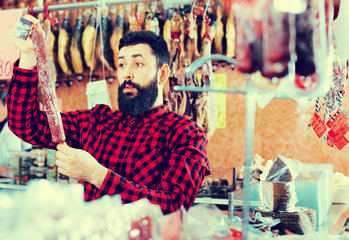 Obraz premium Young male customer examining sausages in butcher’s shop