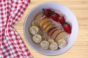 Oat Flakes with sliced bananas and honey, apples and strawberries in bowl. Wood background. Top view.