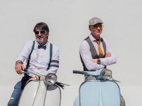 Positive middle-aged hipsters in elegant clothes with retro motorbikes looking away in sunny day