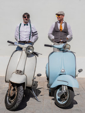 Dreamy middle-aged hipsters in fashionable clothes with retro motorbikes leaning on wall in sunny day