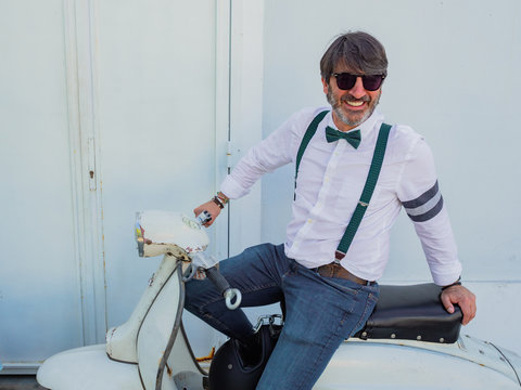Positive middle-aged hipster in elegant clothes with retro motorbikes looking away in sunny day