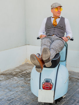 Positive middle-aged hipster in elegant clothes resting on a retro motorbike looking away in sunny day