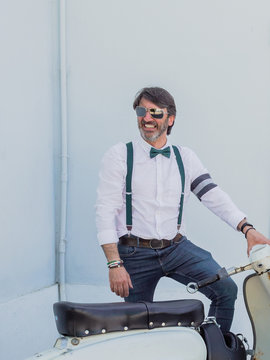 Positive middle-aged hipster in elegant clothes with retro motorbikes looking away in sunny day