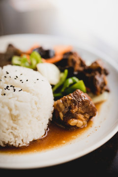 Prepared delicious hot pork ribs with rice and healthy vegetables like cucumber and onion on plate in Asian restaurant