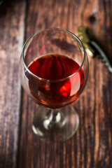 Glass of red wine over rustic, wooden textured table. Dark photo.