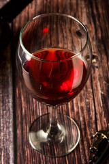 Glass of red wine over rustic, wooden textured table. Dark photo.