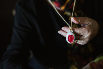Unrecognizable senior female with wrinkled hand demonstrating pendant with emergency button to camera