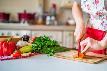 Female hand with knife cuts carrot in kitchen. Cooking vegetables