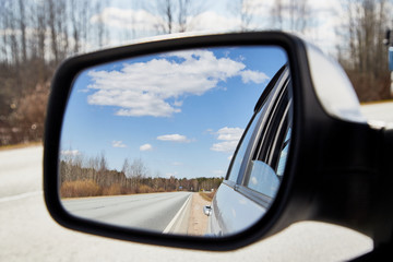 Side view mirror reflection of landscape with road and sky with clouds in sunny spring or autumn day