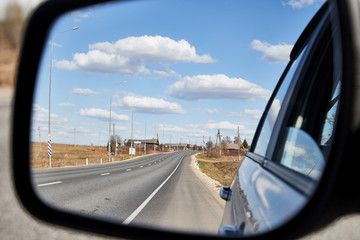 Naklejka premium Side view mirror reflection of landscape with road and sky with clouds in sunny spring or autumn day
