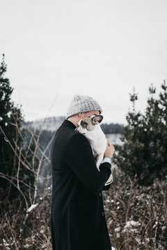 Side view of young woman in casual warm clothes hugging sad cute purebred puppy on mountain in nature